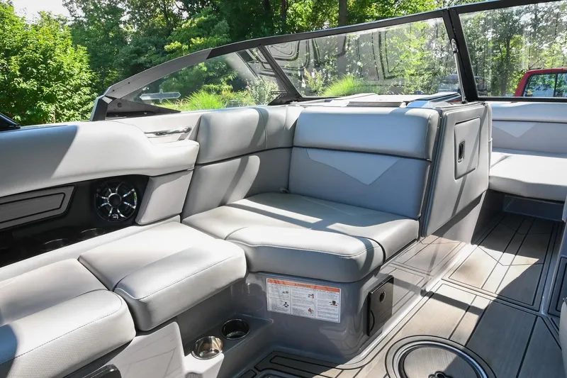 Slide: The Image of 2021 Moomba Kaiyen boat interior with gray seating and cup holders, surrounded by lush greenery. - 23
