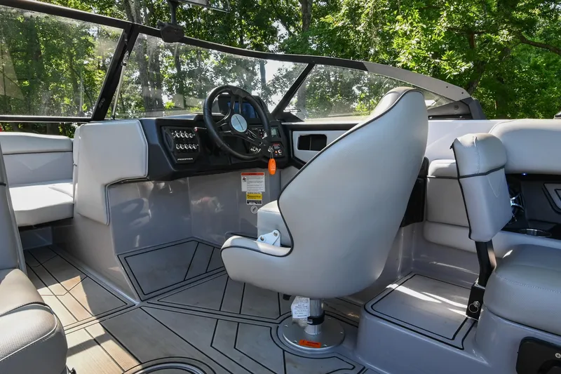 Slide: The Image of 2021 Moomba Kaiyen boat interior with steering wheel and seating, surrounded by lush greenery. - 25