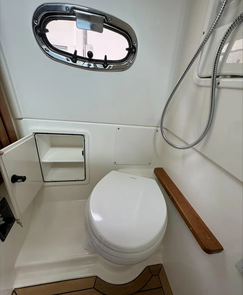 Slide: The Image of 2025 Boston Whaler 380 Outrage bathroom with toilet, porthole, and storage cabinet. - 31