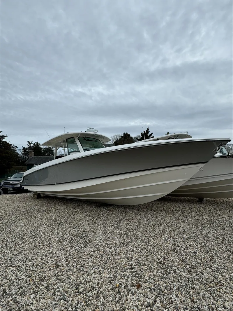 Slide: The Image of 2025 Boston Whaler 380 Outrage boat on gravel under cloudy sky. - 46