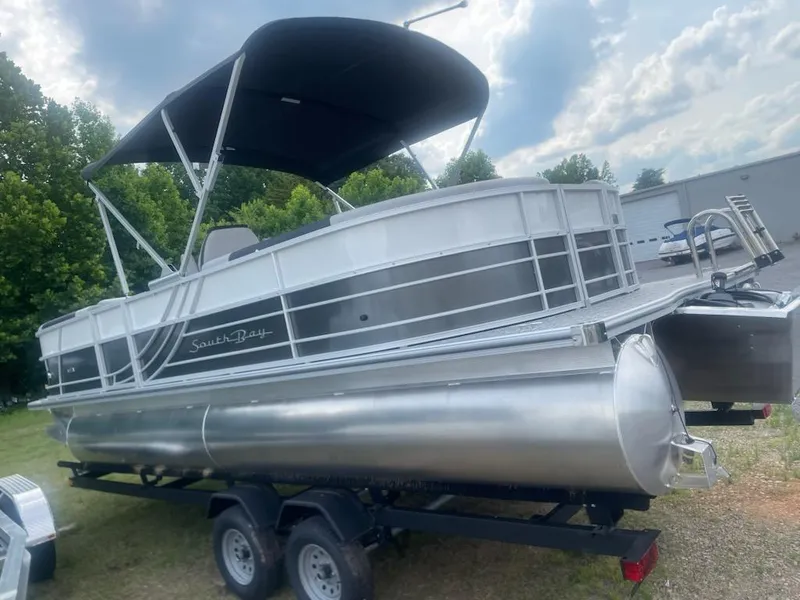 Slide: The Image of 2025 South Bay 224RS LE 2.75 pontoon boat on trailer, under cloudy sky. - 2