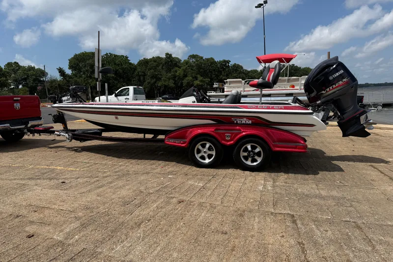 Slide: The Image of 2011 Skeeter FX 21 bass boat on trailer, parked near a lake under a cloudy sky. - 6