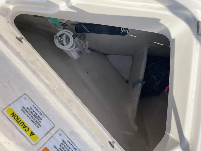 Slide: The Image of Open storage compartment on 2017 Riviera 3600 Sport Yacht with coiled hose and caution labels. - 48