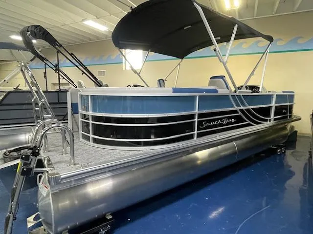 Slide: The Image of 2025 South Bay LE pontoon boat with canopy, displayed indoors on blue flooring. - 1