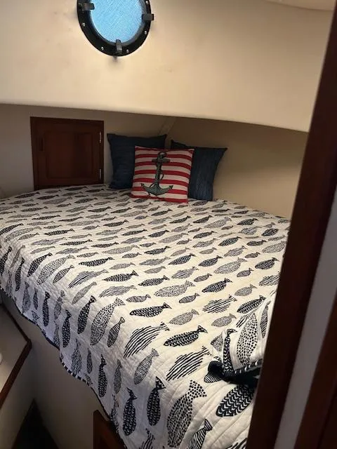 Slide: The Image of Cozy cabin bed in 2001 Nordic Tug 32 with nautical-themed bedding and porthole window. - 12
