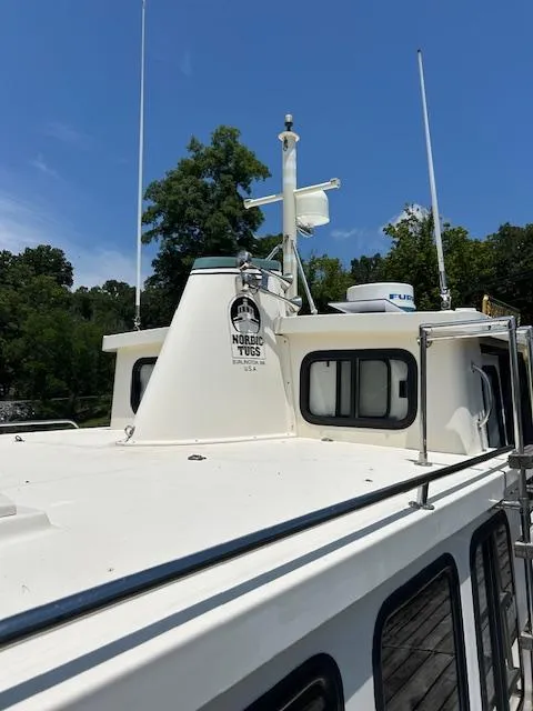 Slide: The Image of 2001 Nordic Tug 32 boat with white exterior, docked near trees under a clear blue sky. - 25