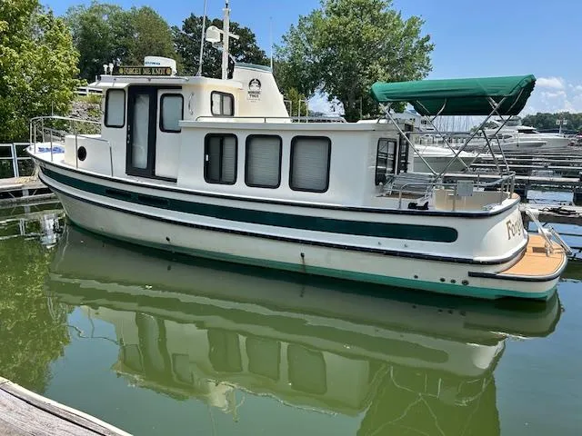 Slide: The Image of 2001 Nordic Tug 32 boat docked on calm water with green canopy and scenic background. - 26
