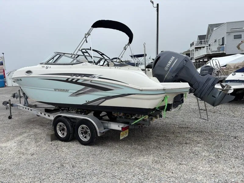 Slide: The Image of 2018 Stingray 214 LR boat on trailer with Yamaha outboard motor, parked on gravel. - 2