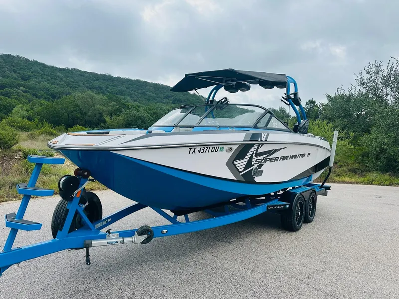 Slide: The Image of 2015 Nautique Super Air Nautique G23 boat on trailer, parked near lush green hills. - 9