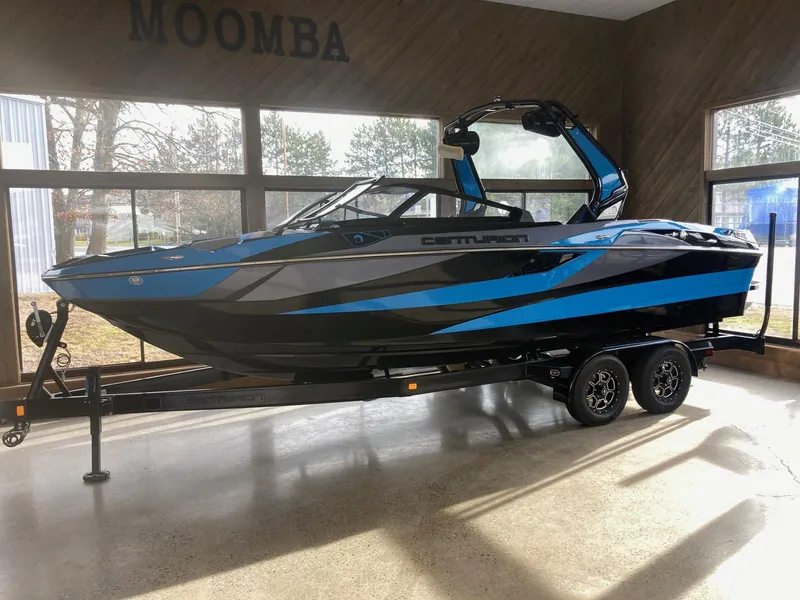 The Image of 2023 Centurion Fi23 boat with blue and black design on a trailer indoors. - 0