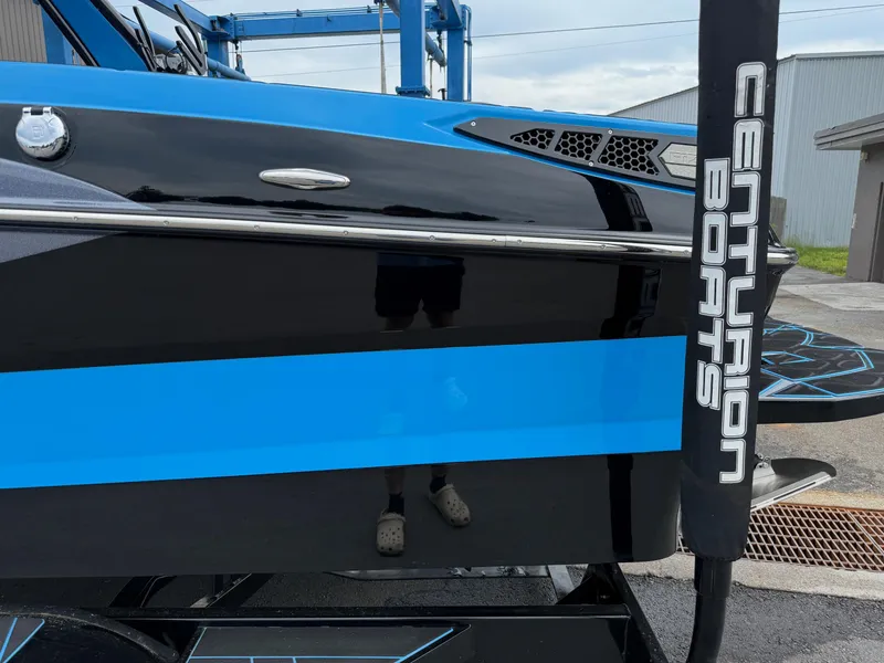 Slide: The Image of 2023 Centurion Fi23 boat with blue and black design, docked outdoors. - 7