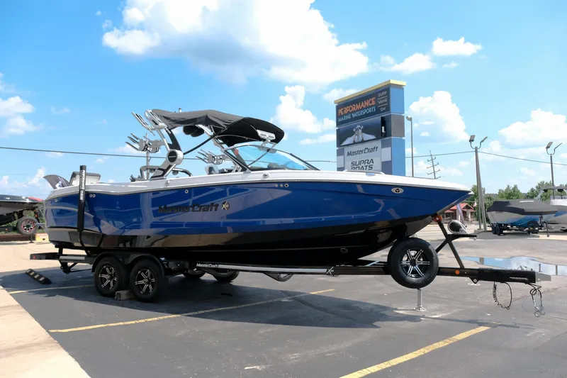 Slide: The Image of 2021 MasterCraft X26 boat on trailer under blue sky at dealership. - 8