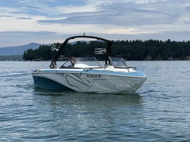 Slide: The Image of 2019 Tigé R21 boat on a calm lake with scenic forested background. - 2