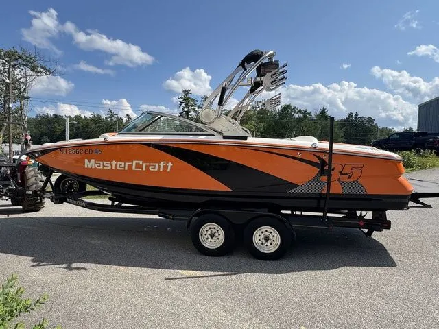 Slide: The Image of 2012 MasterCraft X-35 boat on trailer, orange and black design, parked outdoors under blue sky. - 19