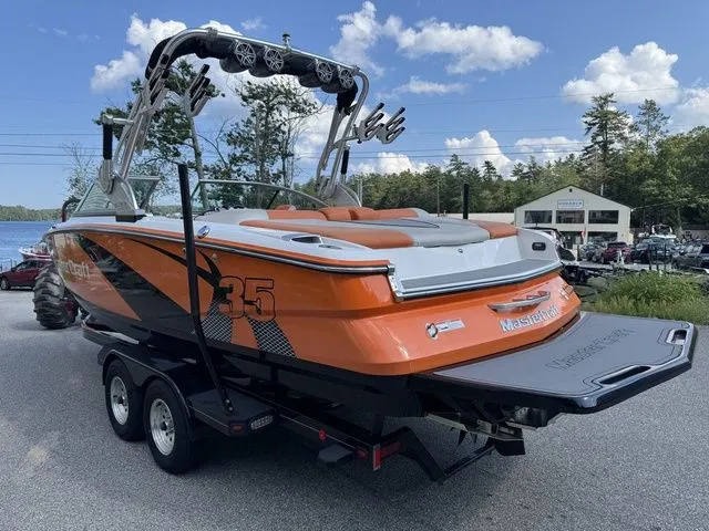 Slide: The Image of 2012 MasterCraft X-35 boat with orange and black design on a trailer, parked outdoors. - 20
