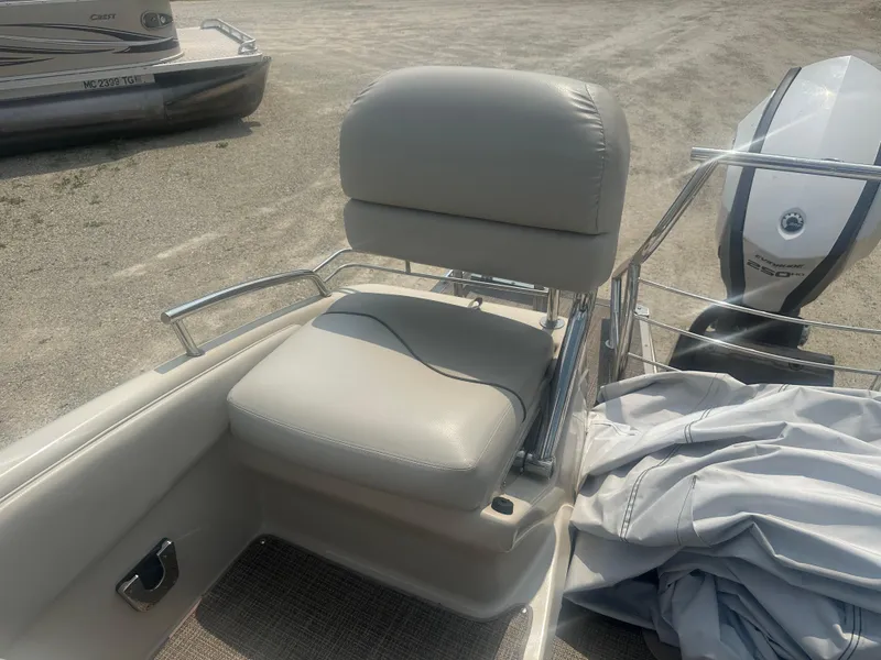 Slide: The Image of 2016 Manitou 25 Legacy SRS boat seat and Evinrude motor on sandy ground. - 6