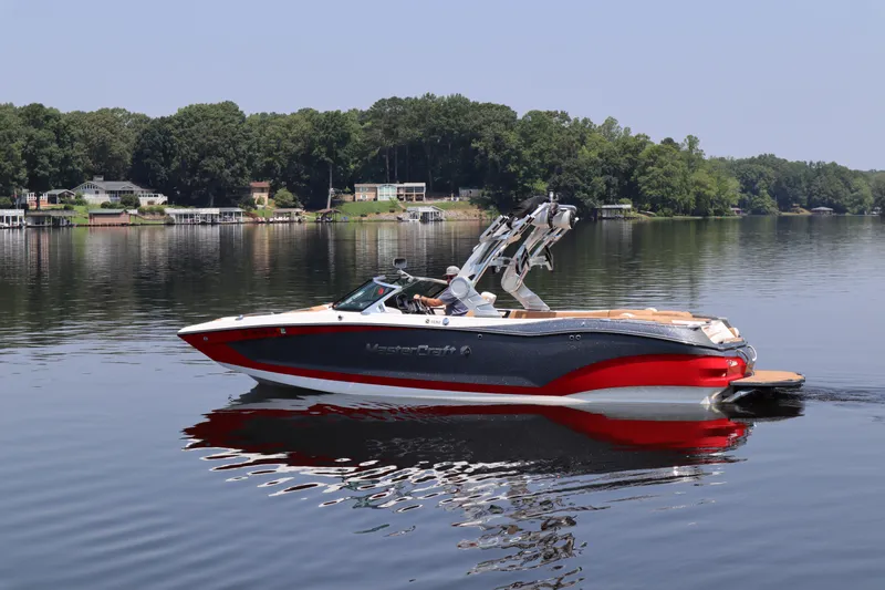 Slide: The Image of 2020 MasterCraft X24 boat cruising on a calm lake with scenic shoreline. - 2