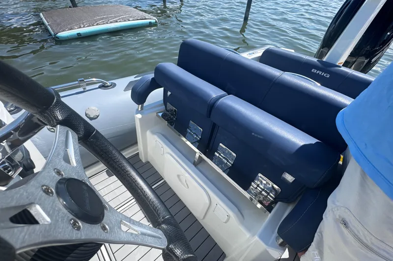 Slide: The Image of 2022 Brig Eagle 6 boat interior with blue seating and steering wheel, docked on water. - 33