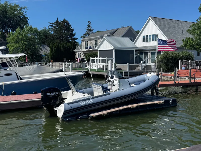 The Image of 2022 Brig Eagle 6 boat docked near waterfront homes, featuring Suzuki outboard motor. - 0
