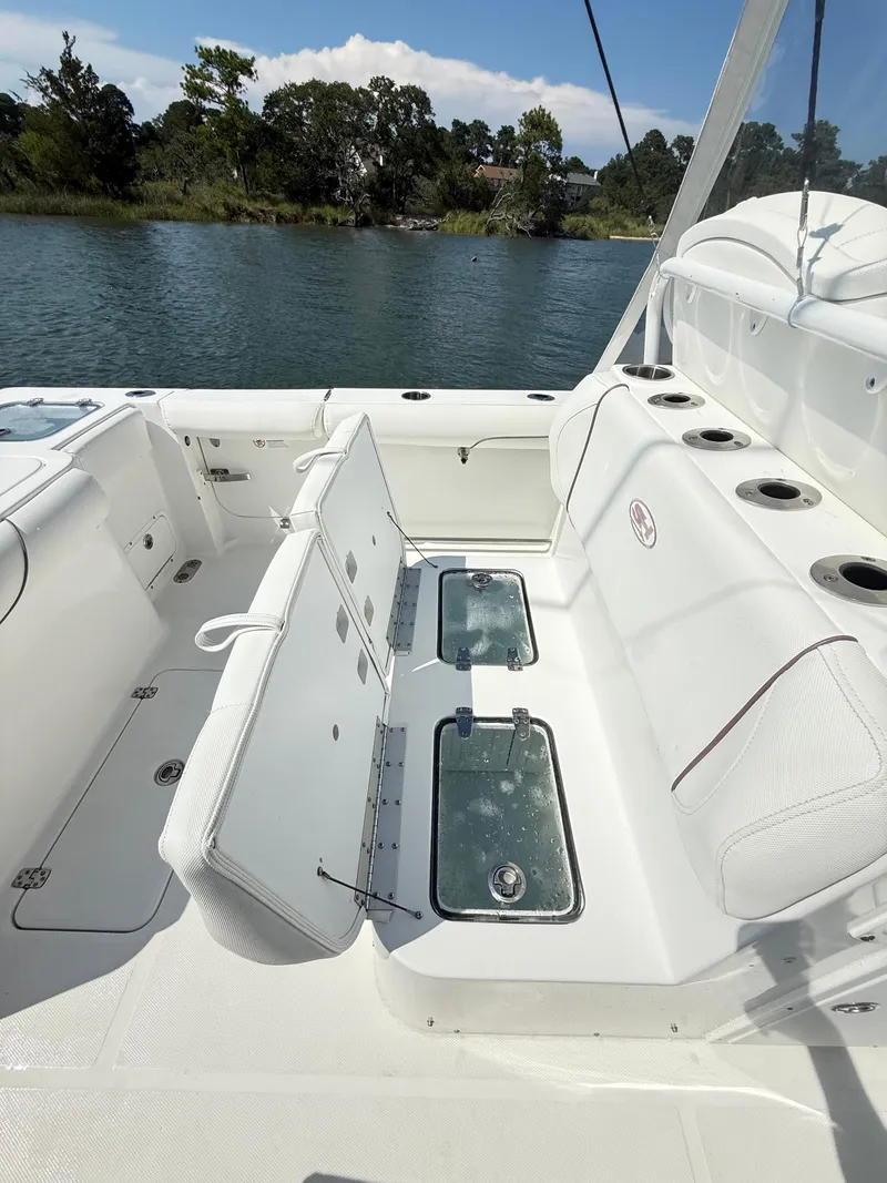 Slide: The Image of 2018 Sea Hunt Gamefish 30 boat with forward seating and live wells, docked by a scenic shoreline. - 31