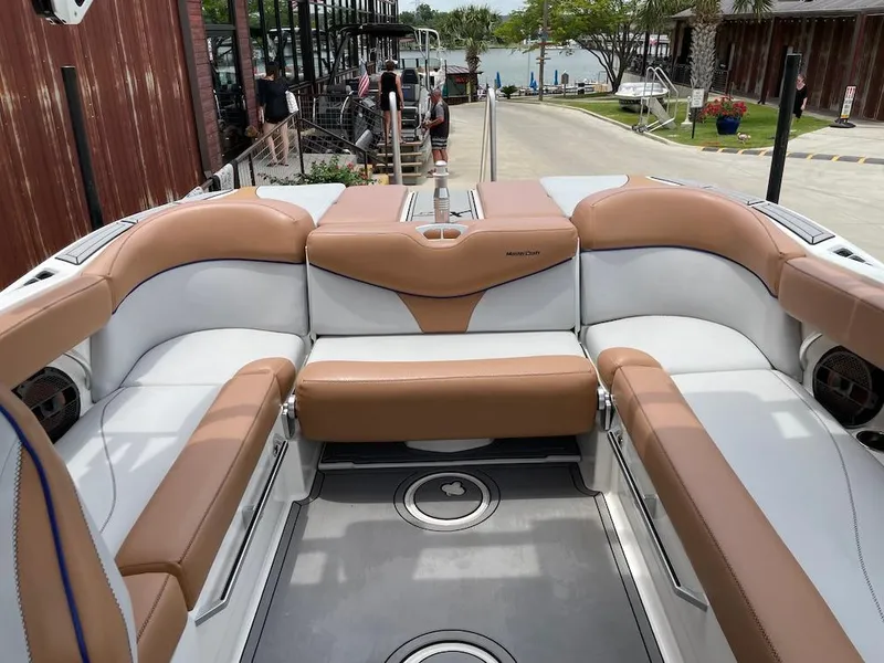 Slide: The Image of 2019 MasterCraft XT23 boat interior with tan and white seating, dockside view. - 16