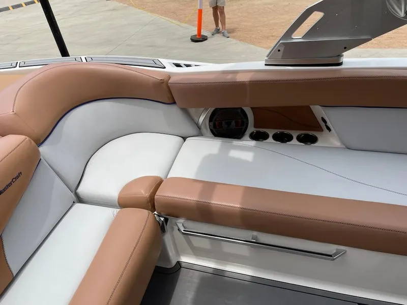 Slide: The Image of 2019 MasterCraft XT23 boat interior with tan and white seating, cup holders, and speaker. - 18
