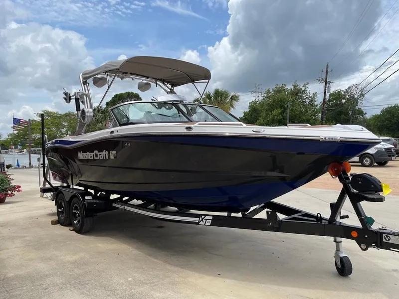 Slide: The Image of 2019 MasterCraft XT23 boat on trailer, parked outdoors under cloudy sky. - 2