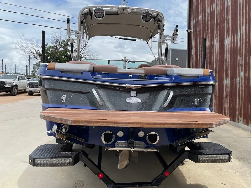 Slide: The Image of 2019 MasterCraft XT23 boat, blue exterior, parked outdoors near a metal building. - 3