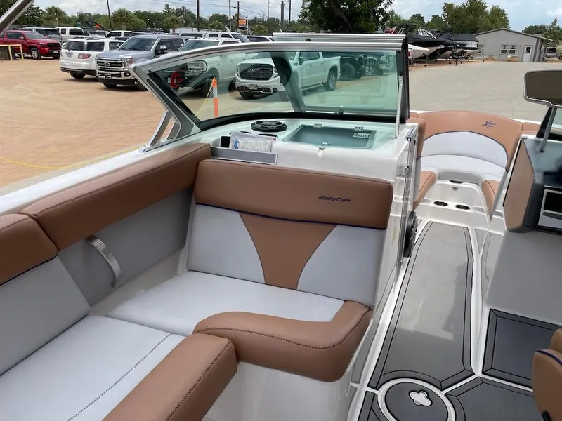 Slide: The Image of 2019 MasterCraft XT23 boat interior with tan and white seating, parked in a lot. - 6