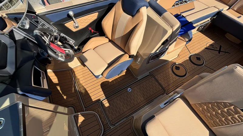 Slide: The Image of 2022 MasterCraft X26 boat interior with tan and navy seating, sleek dashboard, and wood-patterned flooring. - 14