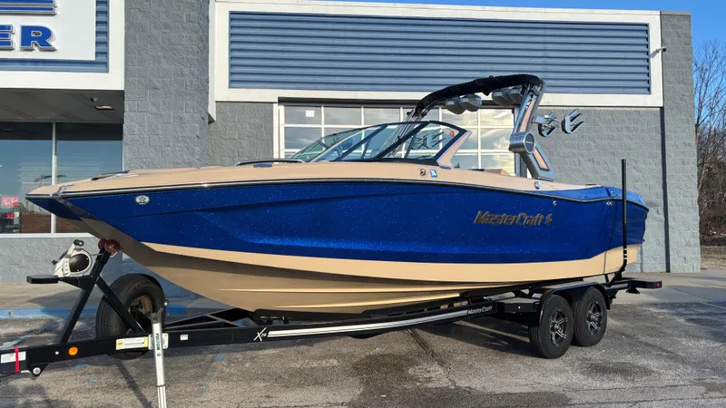 Slide: The Image of 2022 MasterCraft X26 boat in blue and beige on a trailer outside a building. - 2