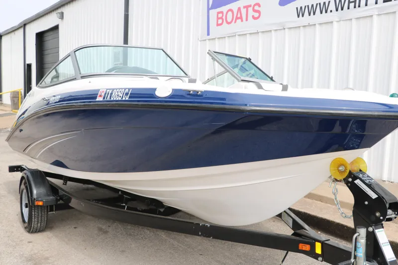 Slide: The Image of 2014 Yamaha Boats SX190 on trailer, blue and white hull, parked outside a building. - 5