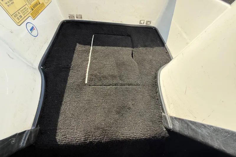 Slide: The Image of 2004 Skeeter ZX250 boat interior with black carpet and visible storage compartment. - 53