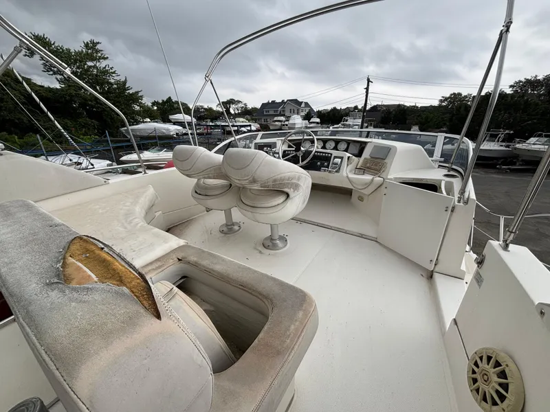 Slide: The Image of 2004 Silverton 35 Motor Yacht cockpit with worn seating and control panel, under cloudy skies. - 4