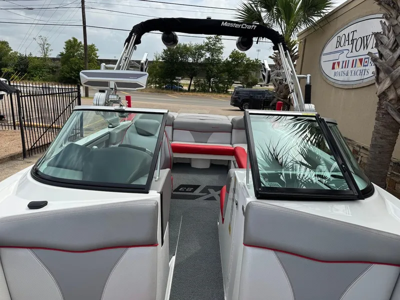 Slide: The Image of 2018 MasterCraft XT23 boat interior with red and gray seating, open windshield, and tower speakers. - 12