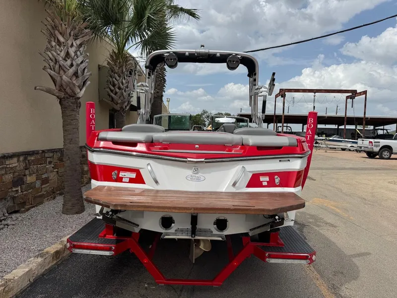 Slide: The Image of 2018 MasterCraft XT23 boat, red and white, parked near palm trees under a cloudy sky. - 3
