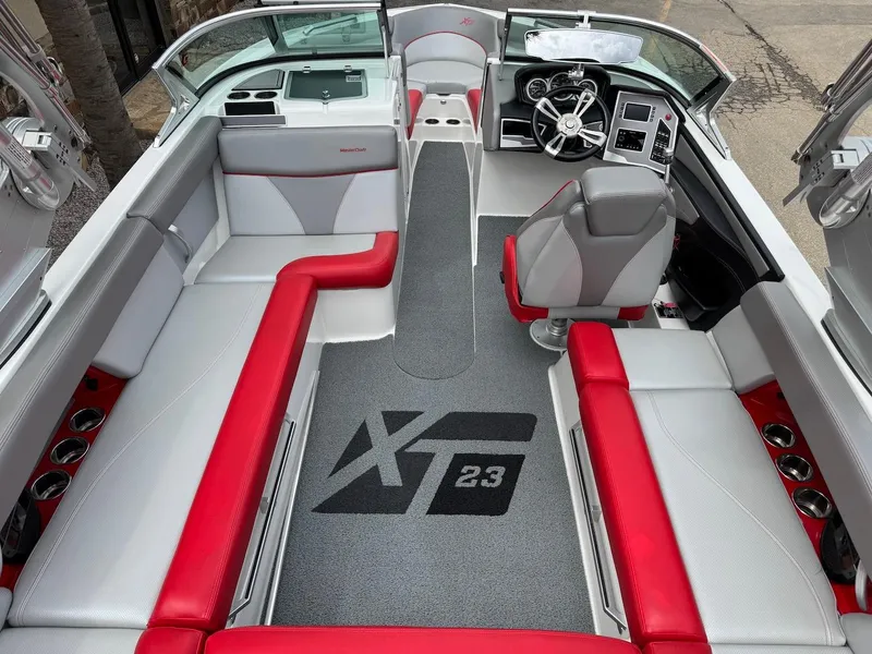 Slide: The Image of 2018 MasterCraft XT23 boat interior with red and gray seating, modern dashboard, and cup holders. - 7