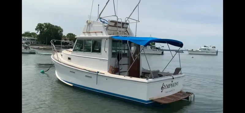 Slide: The Image of 1986 Cape Dory 26 Fly boat with blue canopy, docked in calm waters. - 10