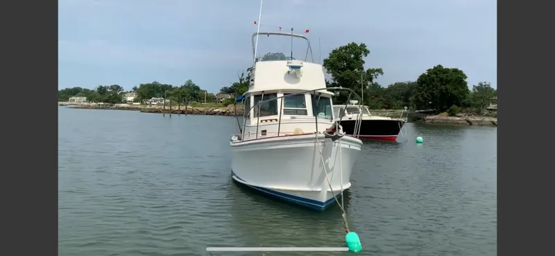 Slide: The Image of 1986 Cape Dory 26 Fly boat moored on calm water, with trees and shoreline in background. - 7
