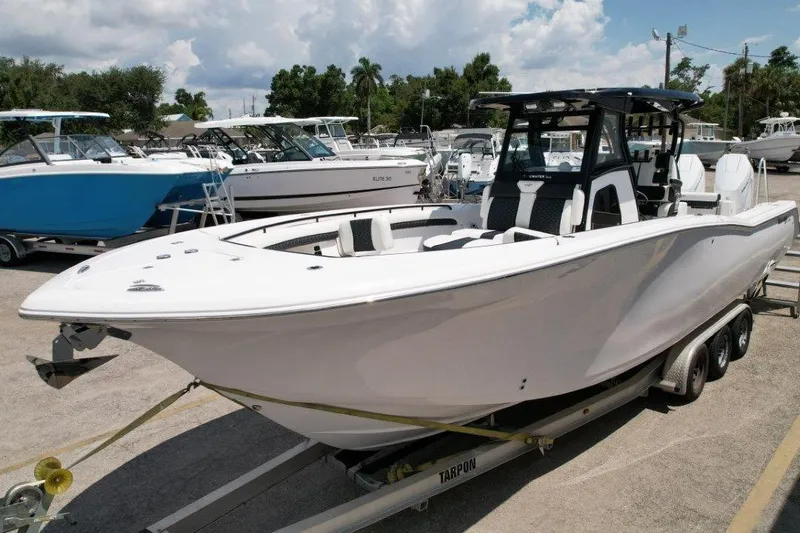 Slide: The Image of 2025 Tidewater 320 CC Adventure boat on trailer, parked in marina under cloudy sky. - 6