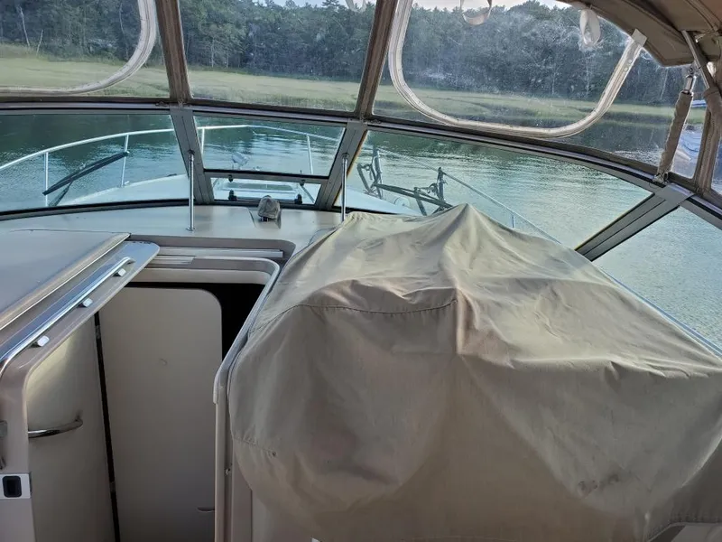 Slide: The Image of 2000 Sea Ray 310 Sundancer interior with covered helm, overlooking calm waters and forested shoreline. - 5