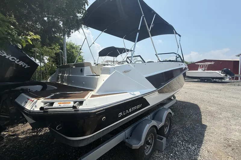 Slide: The Image of 2022 Glastron GTD 220 boat on trailer, featuring sleek design and canopy, parked outdoors. - 16