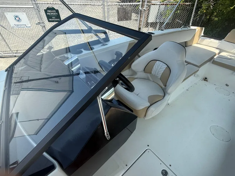 Slide: The Image of 2022 Glastron GTD 220 boat interior with steering wheel and seating, parked near a fence. - 8