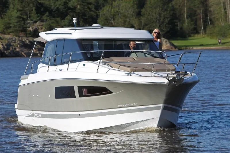 The Image of 2016 Jeanneau NC 9 motor yacht cruising on a lake with forested shoreline. - 0