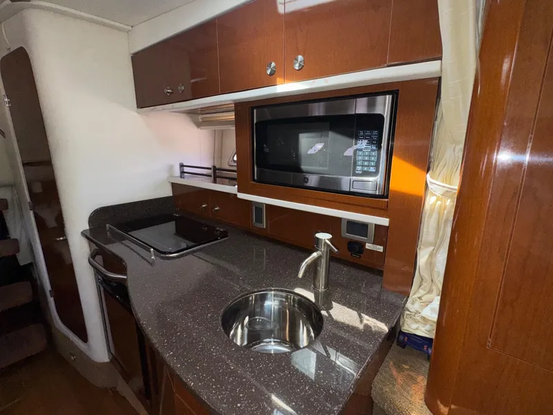 Slide: The Image of 2014 Sea Ray 330 Sundancer galley with microwave, sink, and wooden cabinetry. - 5