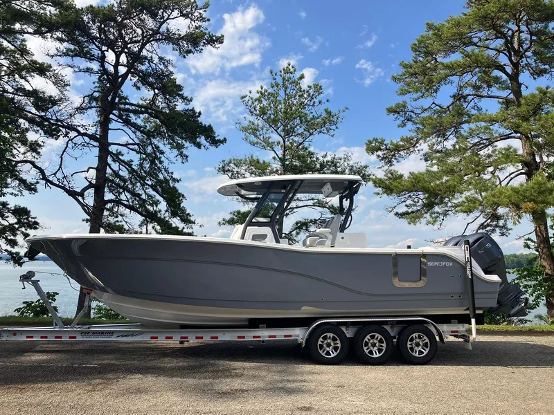 The Image of 2025 Sea Fox 328 Commander boat on trailer, surrounded by trees and blue sky. - 1