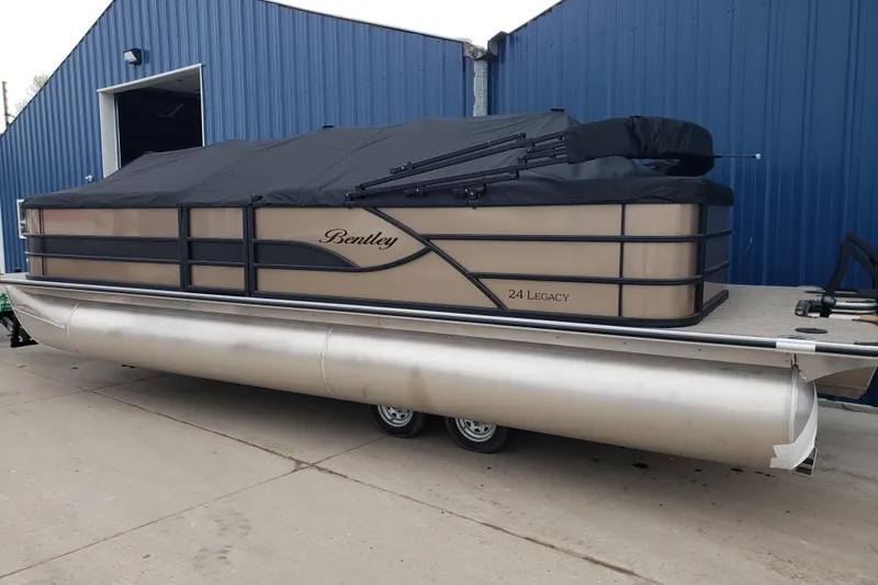 Slide: The Image of 2026 Bentley Pontoons Legacy 243 Cruise pontoon boat with cover, parked outside a blue building. - 6
