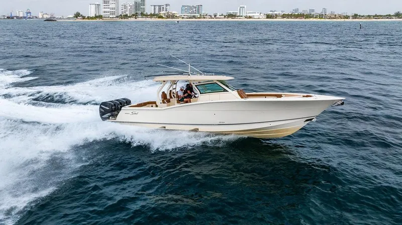 Slide: The Image of 2018 Scout 420 LXF boat cruising on open water near a city skyline. - 10