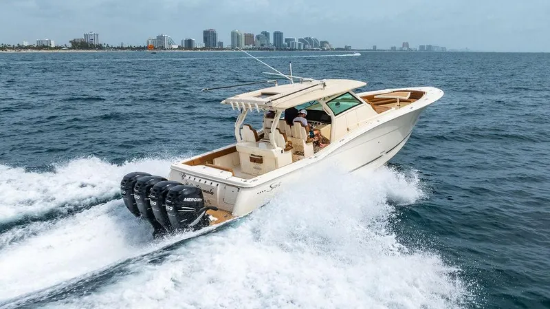 Slide: The Image of 2018 Scout 420 LXF boat cruising on ocean with city skyline in background. - 6