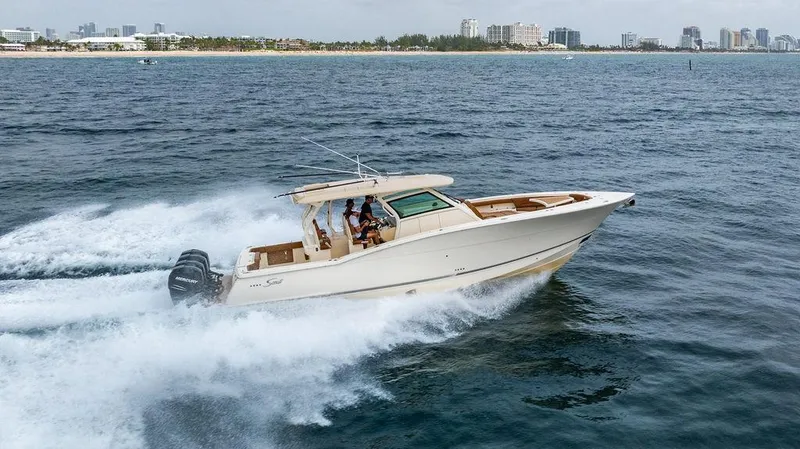 Slide: The Image of 2018 Scout 420 LXF boat cruising on open water near a city skyline. - 9